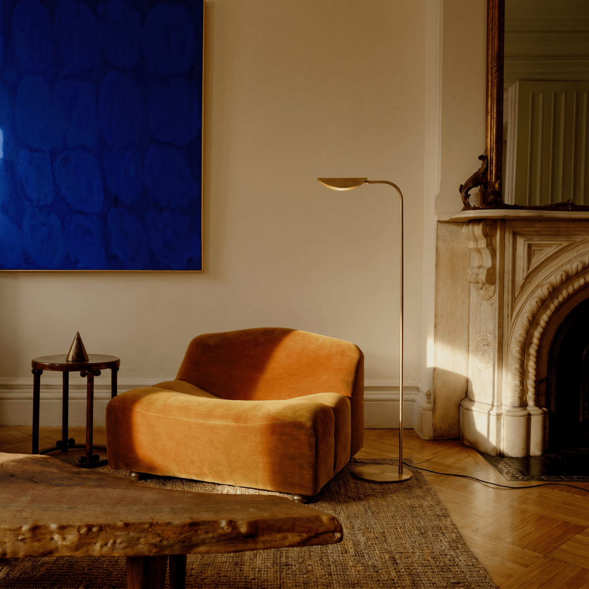 This brass Clérachic floor lamp stands beside an orange velvet armchair near a marble mantel.