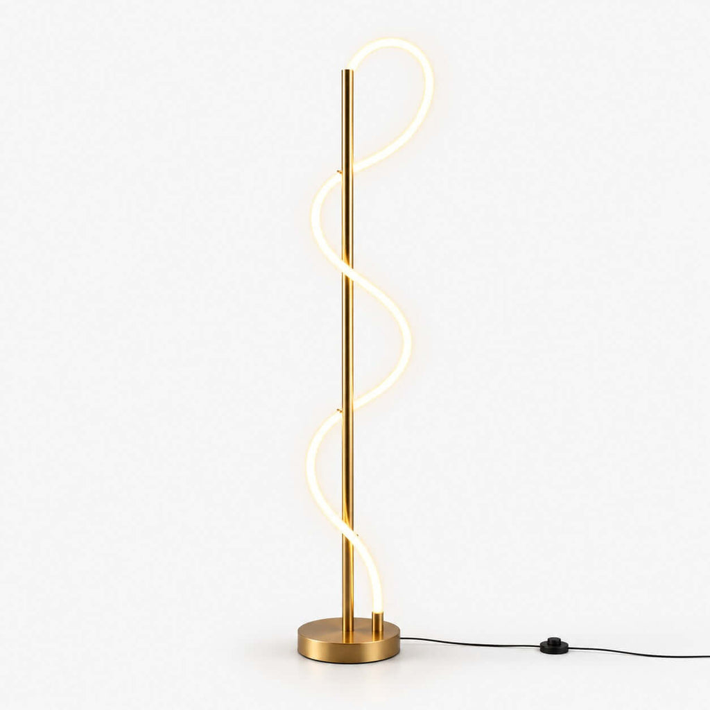 Glowing S-shaped silicone strip curling up a slim brass pole on a round brass base, with a black foot-switch cable on this Clérachic floor lamp.