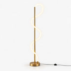 Glowing S-shaped silicone strip curling up a slim brass pole on a round brass base, with a black foot-switch cable on this Clérachic floor lamp.