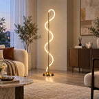 Beside a tall olive plant and a ribbed wooden sideboard at dusk, this Clérachic floor lamp traces a lit curve up its brass pole.