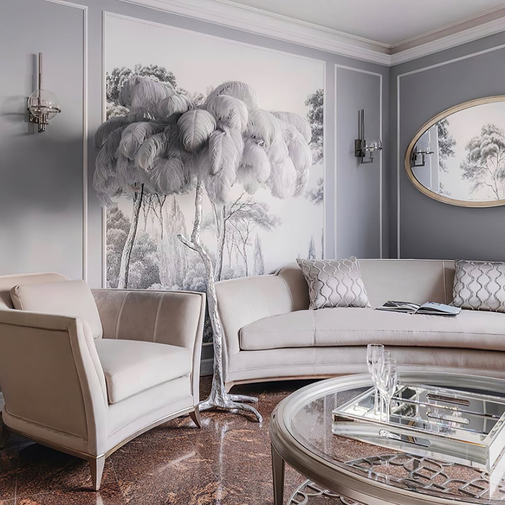 Pale grey plumes spread over a Clérachic floor lamp in a grey sitting room, set against a tree-print mural beside a cream sofa.