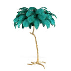 Cut-out view of a teal-feathered Clérachic floor lamp, its textured gold stem branching into a splayed three-footed base.