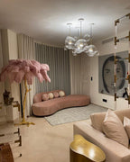 Blush-pink plumes on a Clérachic floor lamp in a pale living room with a curved pink sofa and glass pendant lights.