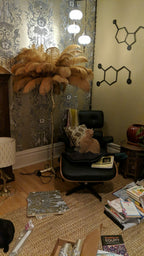 Golden-tan feathers on a Clérachic floor lamp in a busy study with a leather lounge chair and patterned wallpaper.