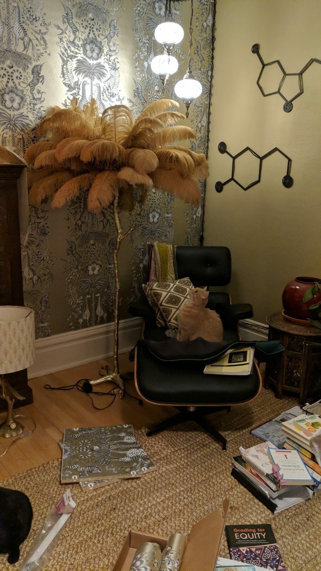Golden-tan feathers on a Clérachic floor lamp in a busy study with a leather lounge chair and patterned wallpaper.