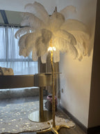White plumes lit from inside on a Clérachic floor lamp, standing in a modern room beside a desk and a patterned rug.