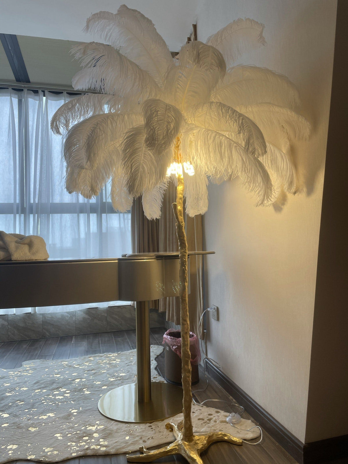 White plumes lit from inside on a Clérachic floor lamp, standing in a modern room beside a desk and a patterned rug.