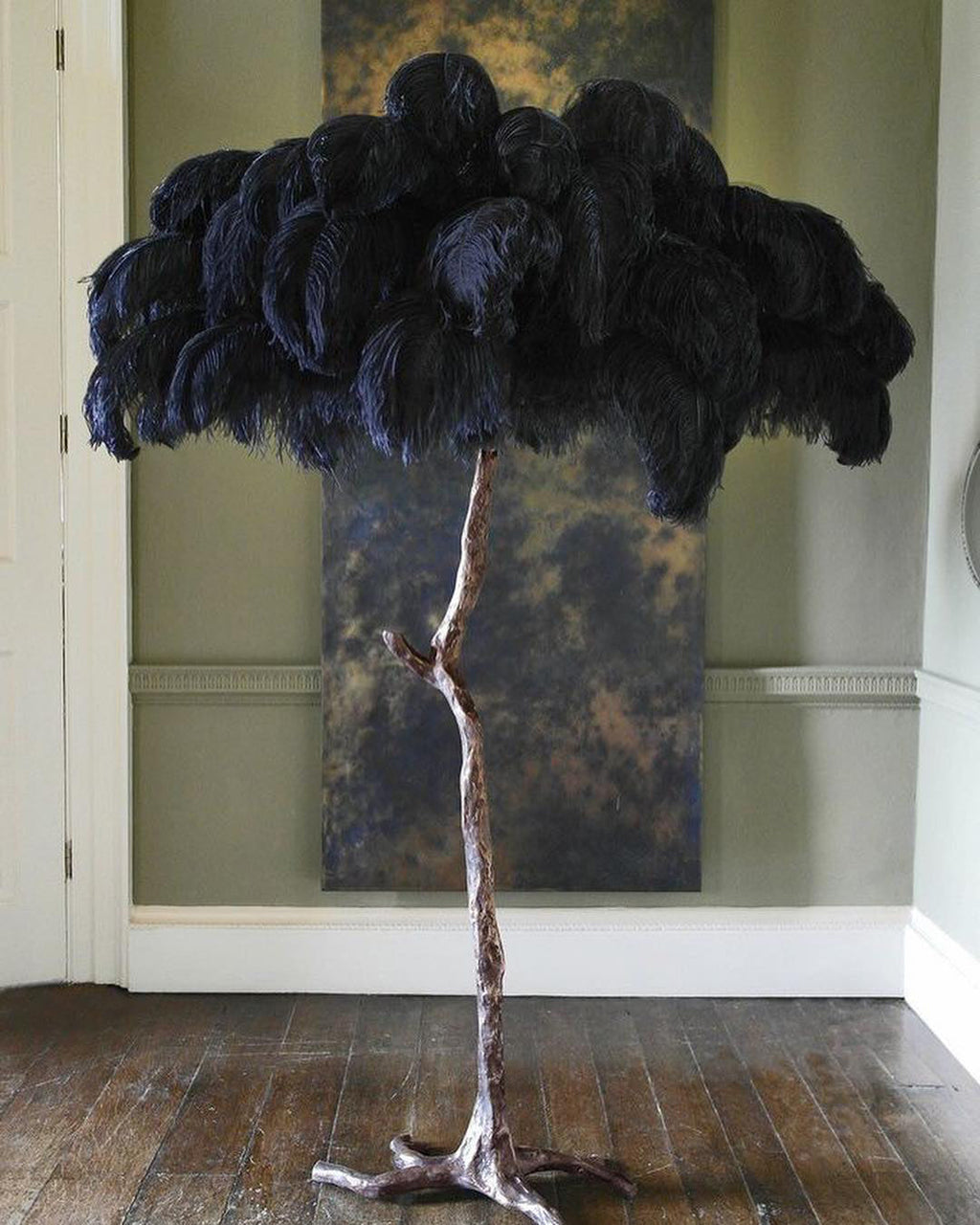 Navy-black plumes on a Clérachic floor lamp with a silver stem, in front of a bronze panel on a sage-green wall.