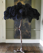 Navy-black plumes on a Clérachic floor lamp with a silver stem, in front of a bronze panel on a sage-green wall.