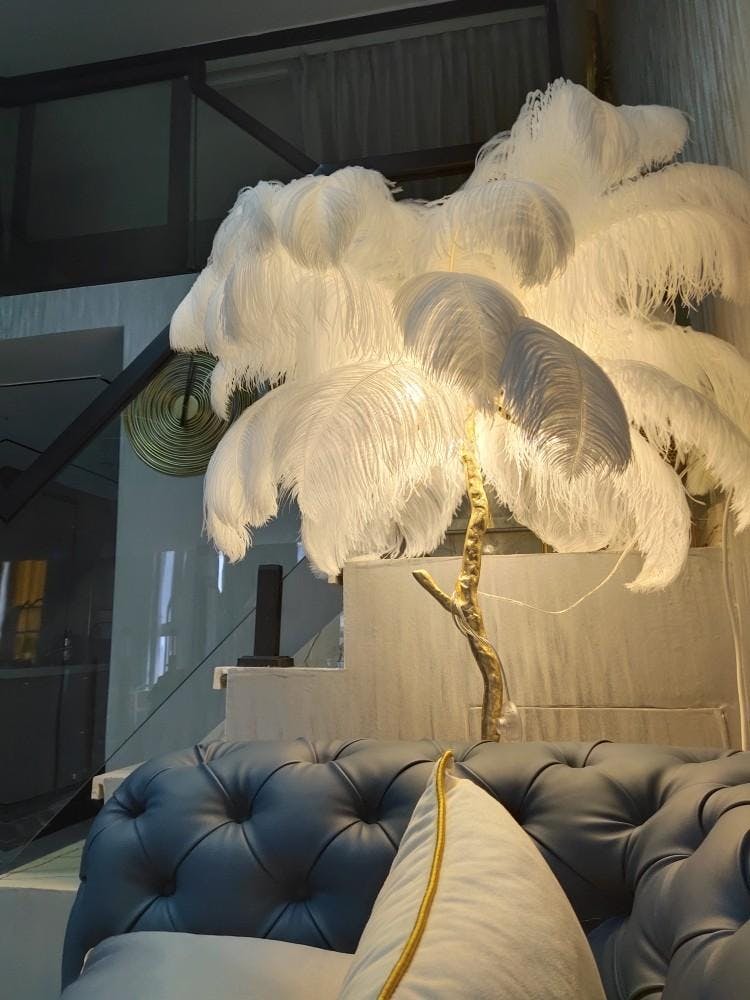 Lit white plumes on a Clérachic floor lamp, glowing over a blue tufted sofa in a loft with a steel staircase.