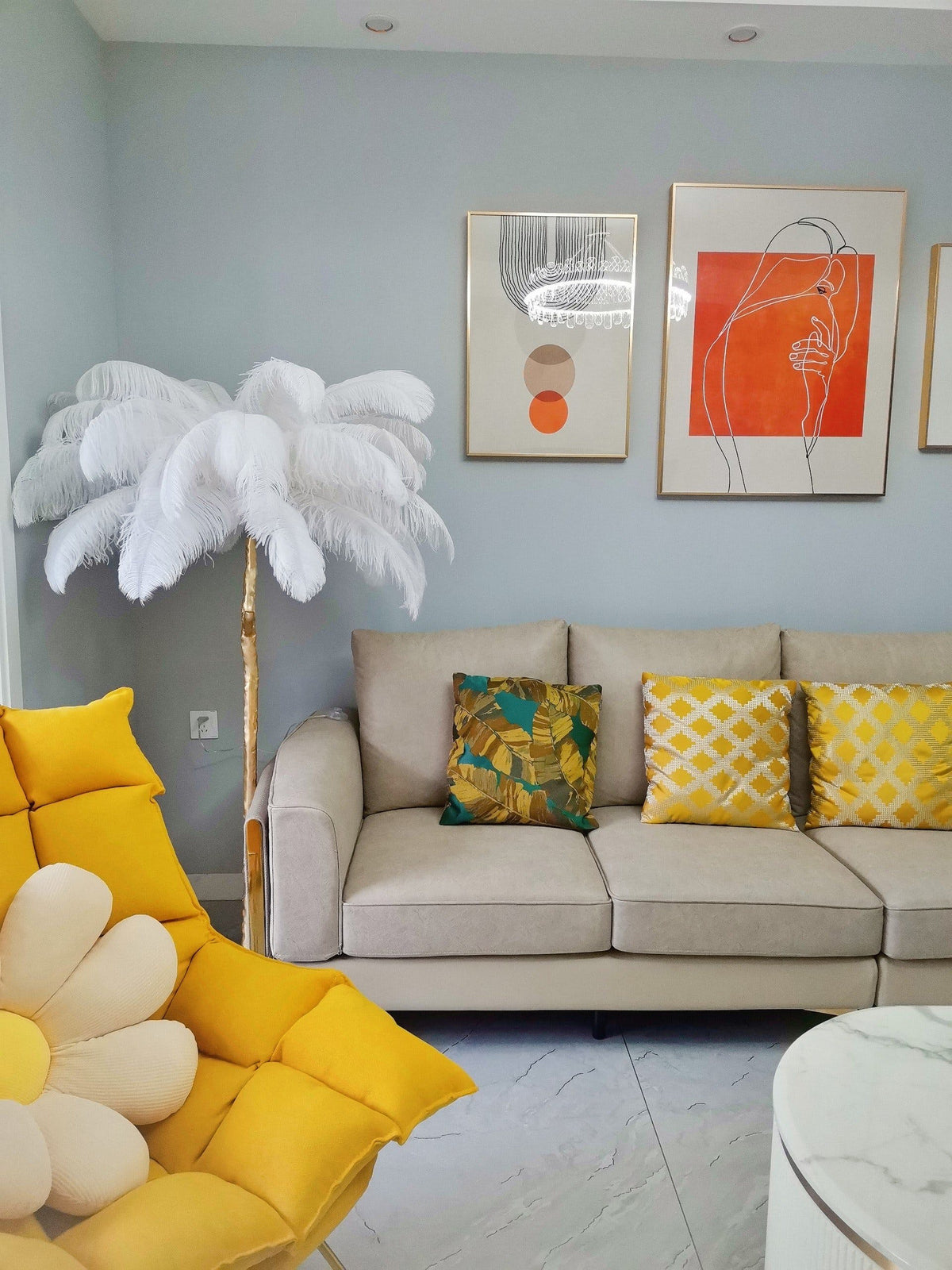 A small white-feathered Clérachic floor lamp stands behind a beige sofa in a pale blue room with a yellow chair.