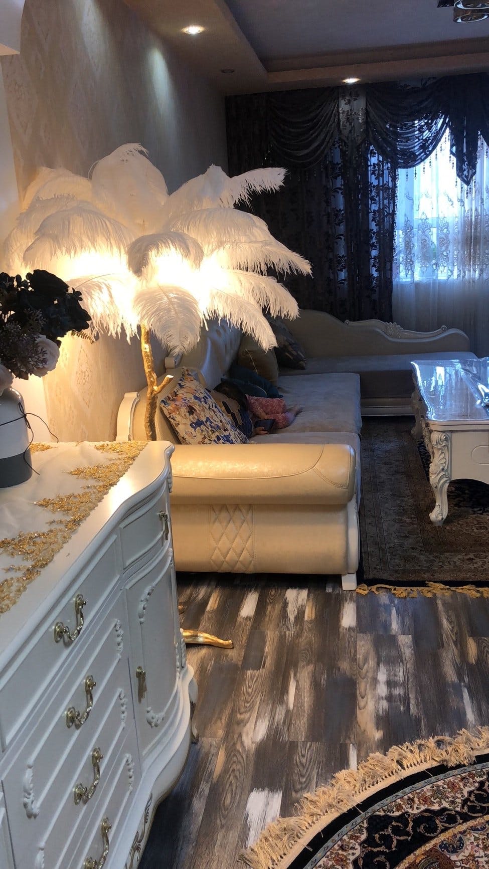 Warm white plumes on a lit Clérachic floor lamp, in a sitting room with a white chest of drawers and patterned rug.
