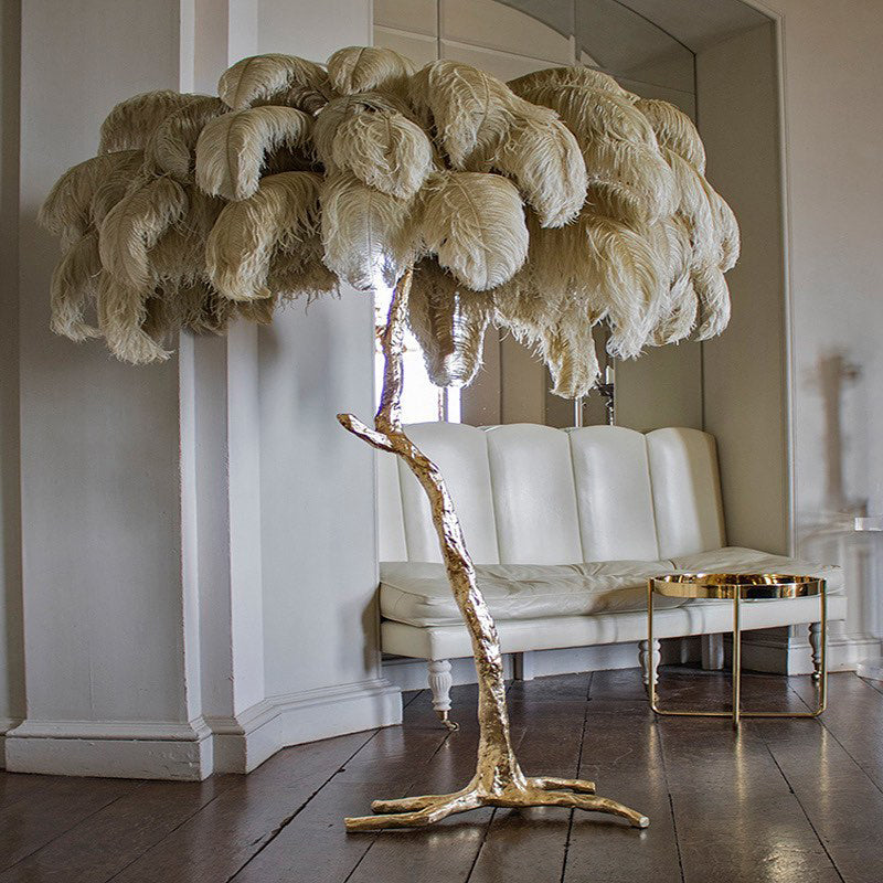 Sand-coloured plumes on a Clérachic floor lamp with a gold branch-like stem, beside a cream leather sofa and a brass tray table.
