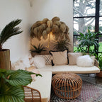 Taupe-gold plumes on a Clérachic floor lamp in a bright sun room with palms, a corner sofa and a rattan pouffe.
