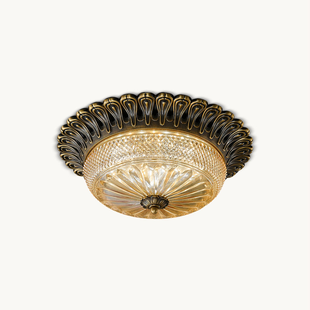 Clérachic flush mount ceiling light in antique brass with a carved scalloped rim and amber glass bowl, on a plain white backdrop.