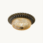 Clérachic flush mount ceiling light in antique brass with a carved scalloped rim and amber glass bowl, on a plain white backdrop.