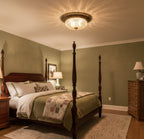 Clérachic flush mount light glowing on the ceiling of a sage-green bedroom, with a patchwork quilt on a dark wood four-poster bed.