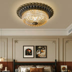 Clérachic brass and amber glass ceiling light above a dark spindle bed, with panelled walls and two framed prints in warm light.