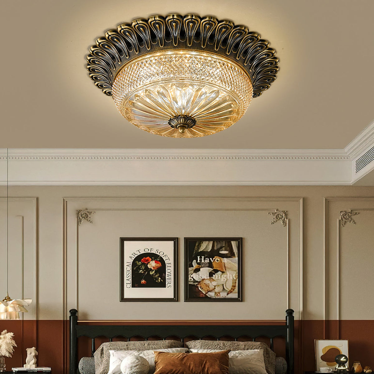 Clérachic brass and amber glass ceiling light above a dark spindle bed, with panelled walls and two framed prints in warm light.