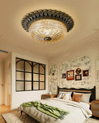 Clérachic flush mount light over a bedroom with floral wallpaper, a dark arched glass panel and a green throw across the bed.