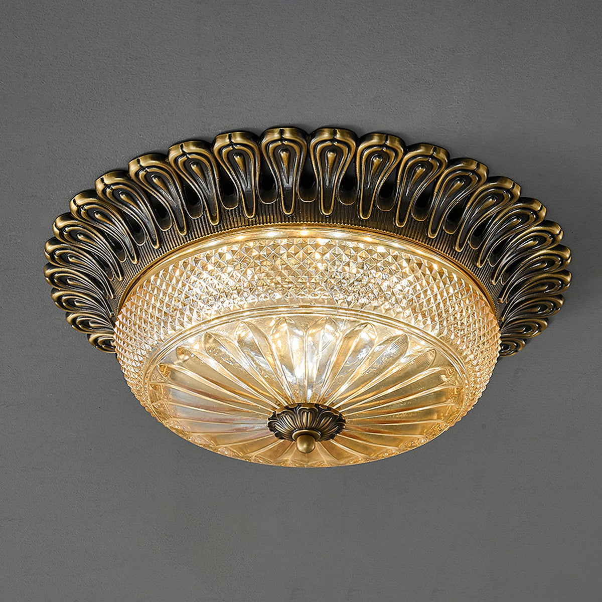 Clérachic flush mount ceiling light seen at an angle on a dark grey backdrop, the carved brass rim over a diamond-cut amber glass bowl.