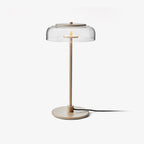 This Clérachic table lamp on a plain white backdrop, with a clear glass dome, a slim brass-toned stem and a round base with a black cord.