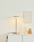 A Clérachic table lamp lit on a white cabinet, with a framed textured artwork and two small ornaments on the wall side.