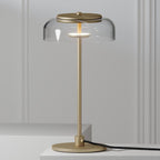 Close view of the clear glass dome and brass-toned cap on a Clérachic table lamp, with its stem and round base on a pale surface.
