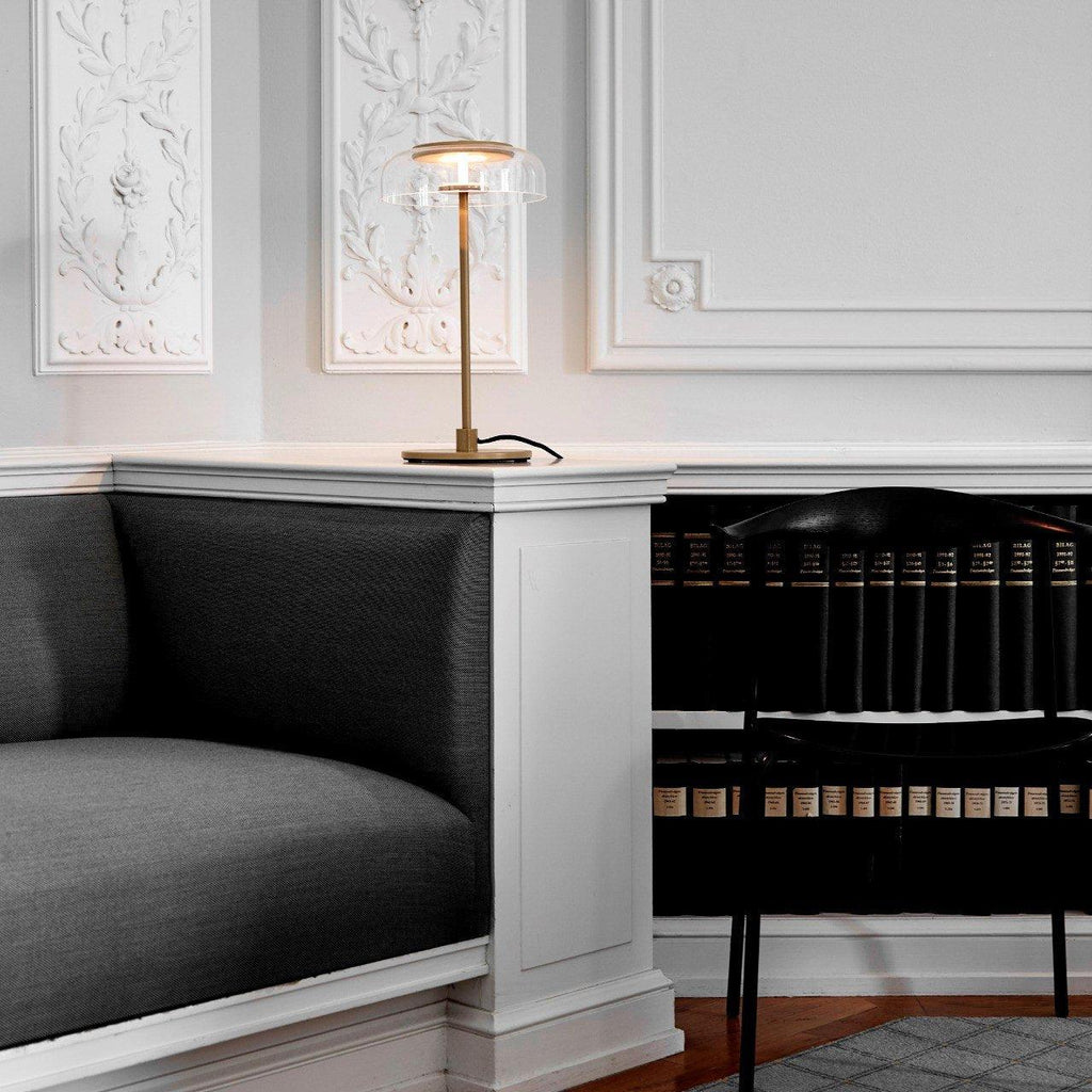 A Clérachic table lamp standing on a white window seat in a panelled room, with a dark bench seat and shelves of books beside it.