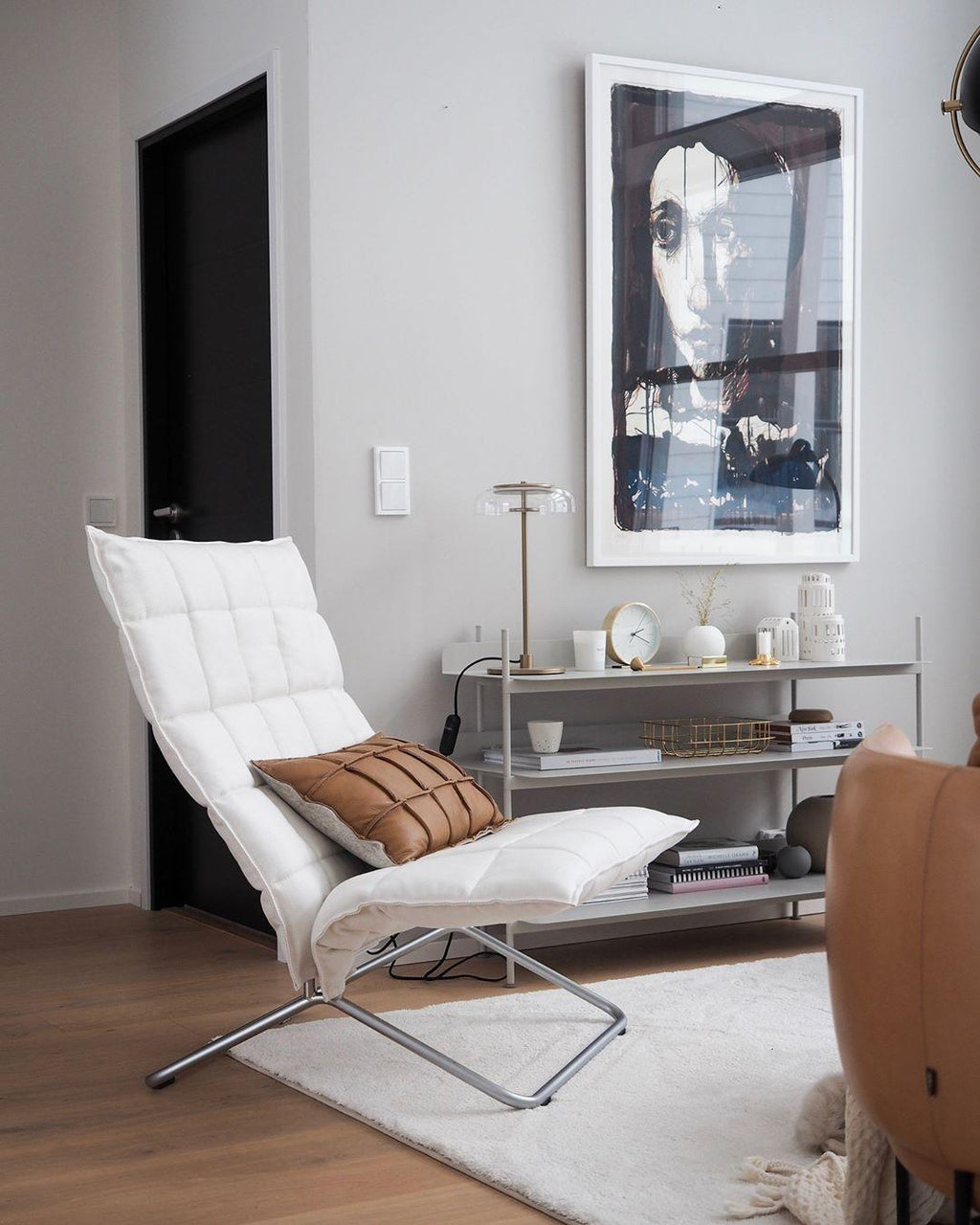 In the corner of a living room with a white lounge chair and a large framed print, a Clérachic table lamp stands on a shelf unit.