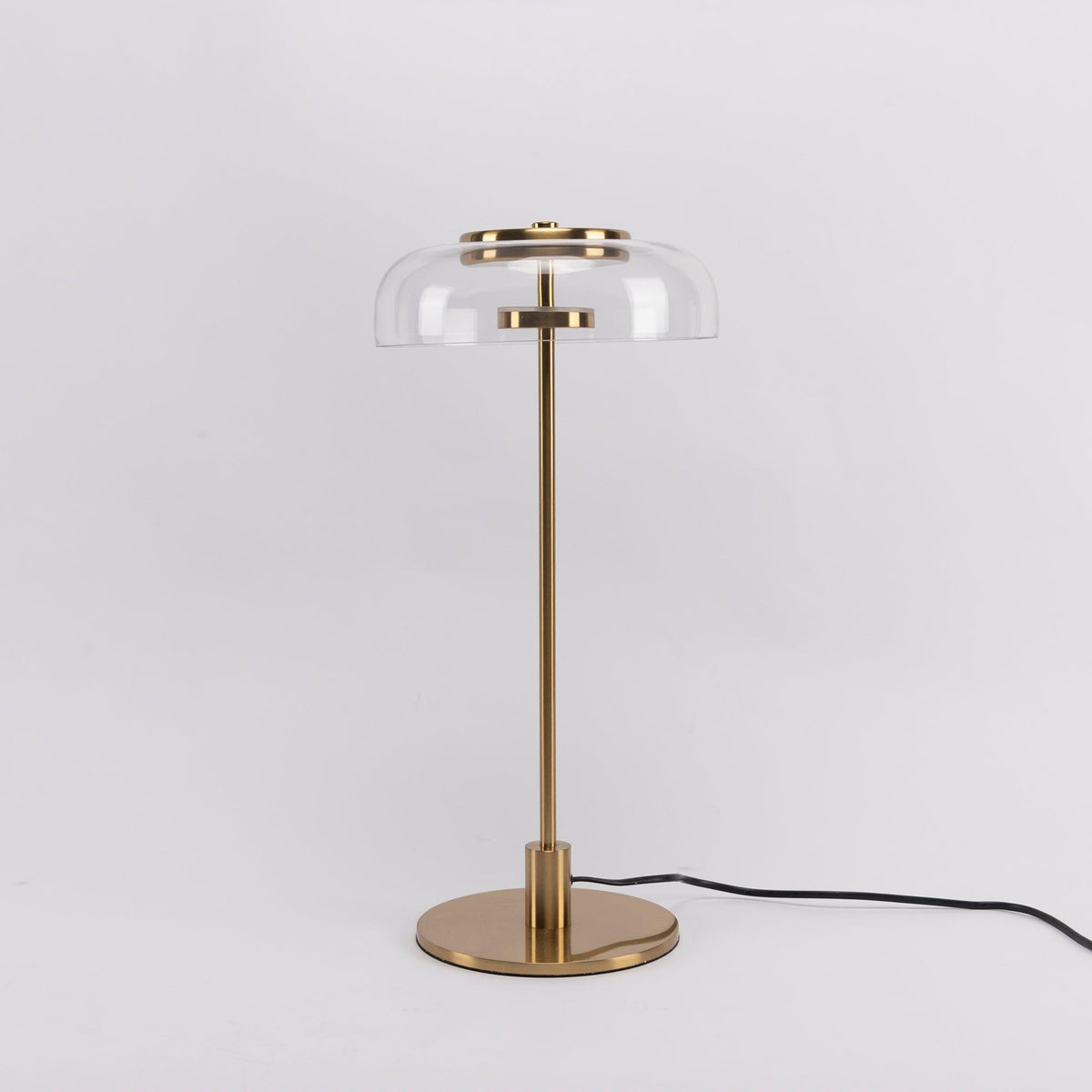 This Clérachic table lamp on a plain pale grey backdrop, with a clear glass dome, a brass stem and a cable running off to the right.