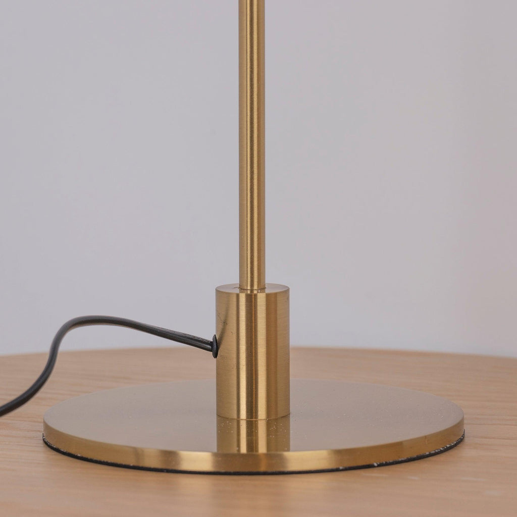 Close view of the brass collar and the round base of this Clérachic table lamp, on a wooden surface with the black cord trailing away.