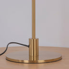 Close view of the brass collar and the round base of this Clérachic table lamp, on a wooden surface with the black cord trailing away.
