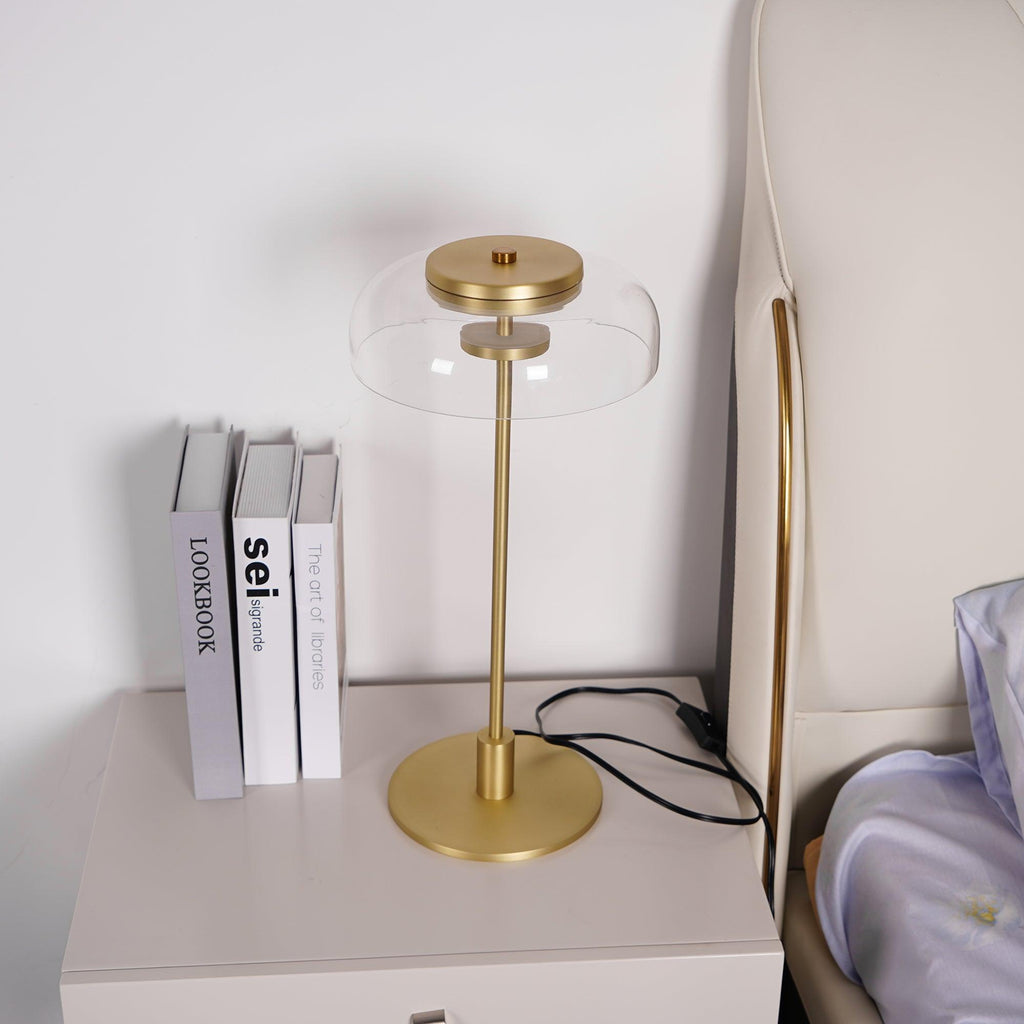 A closer view of this Clérachic table lamp on a bedside chest, with its brass base and a clear dome, next to three books.