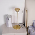A closer view of this Clérachic table lamp on a bedside chest, with its brass base and a clear dome, next to three books.