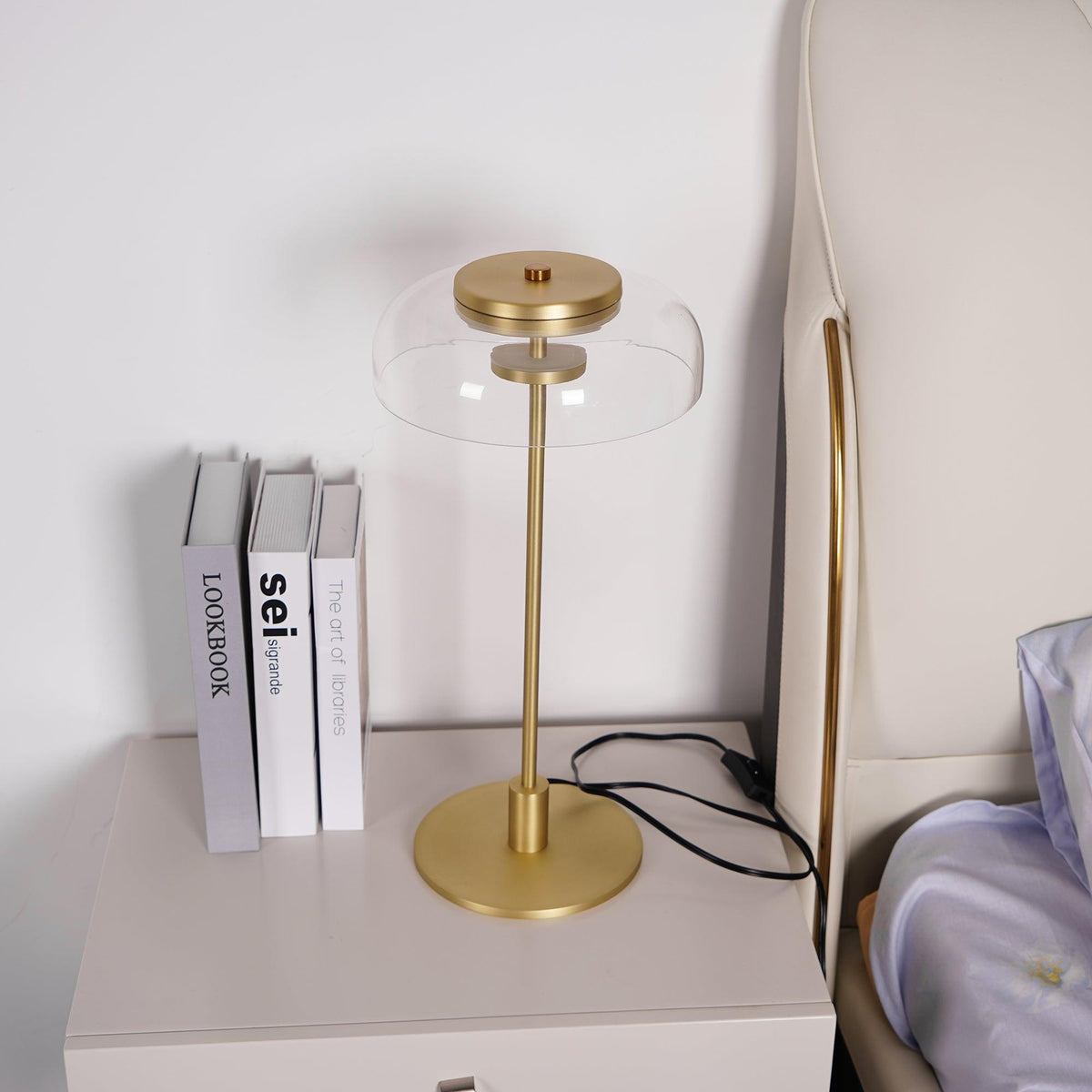 A closer view of this Clérachic table lamp on a bedside chest, with its brass base and a clear dome, next to three books.