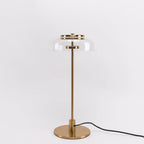A Clérachic table lamp with a clear glass dome and brass stem on a pale grey backdrop, shown full length with its cord.