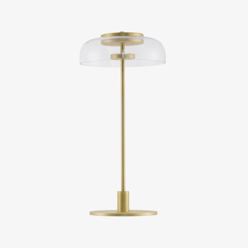 A Clérachic table lamp with a clear dome and a slim stem on a white background, with a flat, round brass-toned base.
