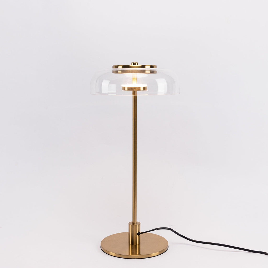 A Clérachic table lamp with a darker brass finish, shown on a pale backdrop with a clear dome and a cord trailing to the right.