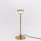 A Clérachic table lamp with a darker brass finish, shown on a pale backdrop with a clear dome and a cord trailing to the right.