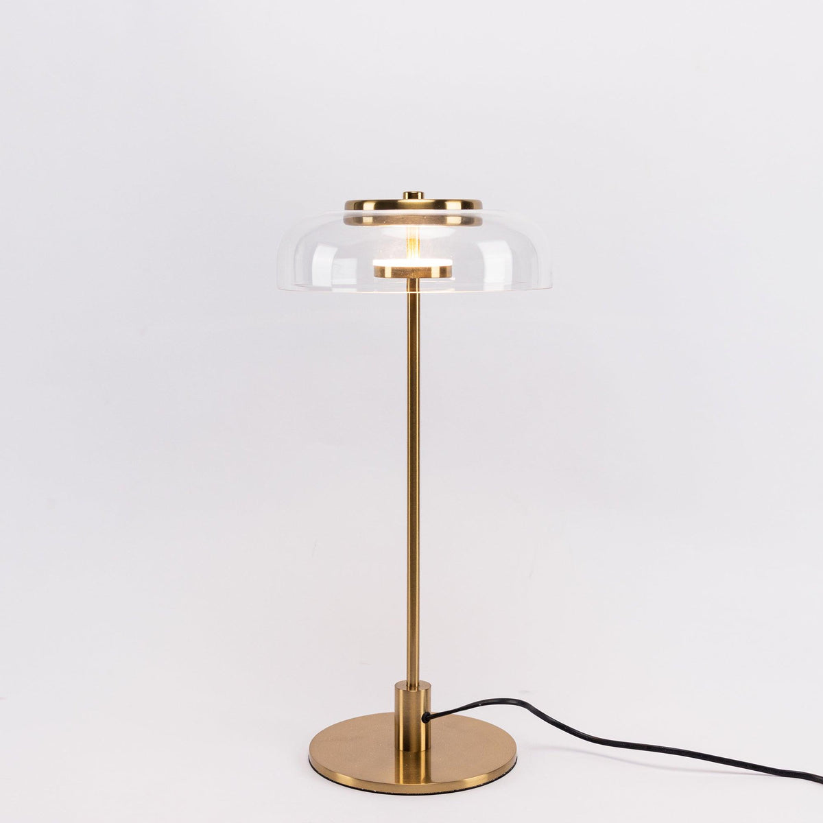 A Clérachic table lamp with a darker brass finish, shown on a pale backdrop with a clear dome and a cord trailing to the right.