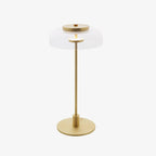 Clérachic table lamp shown on a pale grey backdrop, with a clear glass dome, a brass cap and a brass stem on a round base.