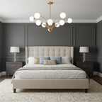 A Clérachic brass chandelier with white glass globes over a bed with a cream tufted headboard, in a charcoal panelled bedroom.