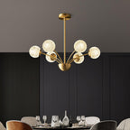 A Clérachic chandelier with textured globes over a dining table set with glasses, in front of dark fluted wall panelling.