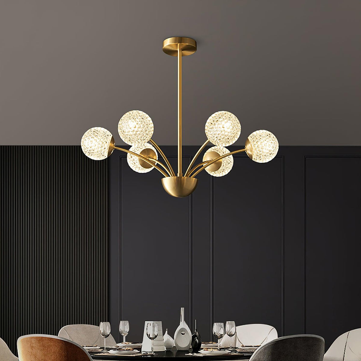 A Clérachic chandelier with textured globes over a dining table set with glasses, in front of dark fluted wall panelling.
