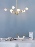 A Clérachic brass chandelier with textured globes lit against a pale blue wall, with a white-clothed table and a vase below.