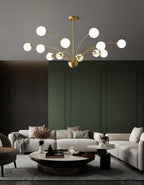 A Clérachic chandelier with white globes in a living room with a dark green panelled wall, a cream sofa and a round coffee table.