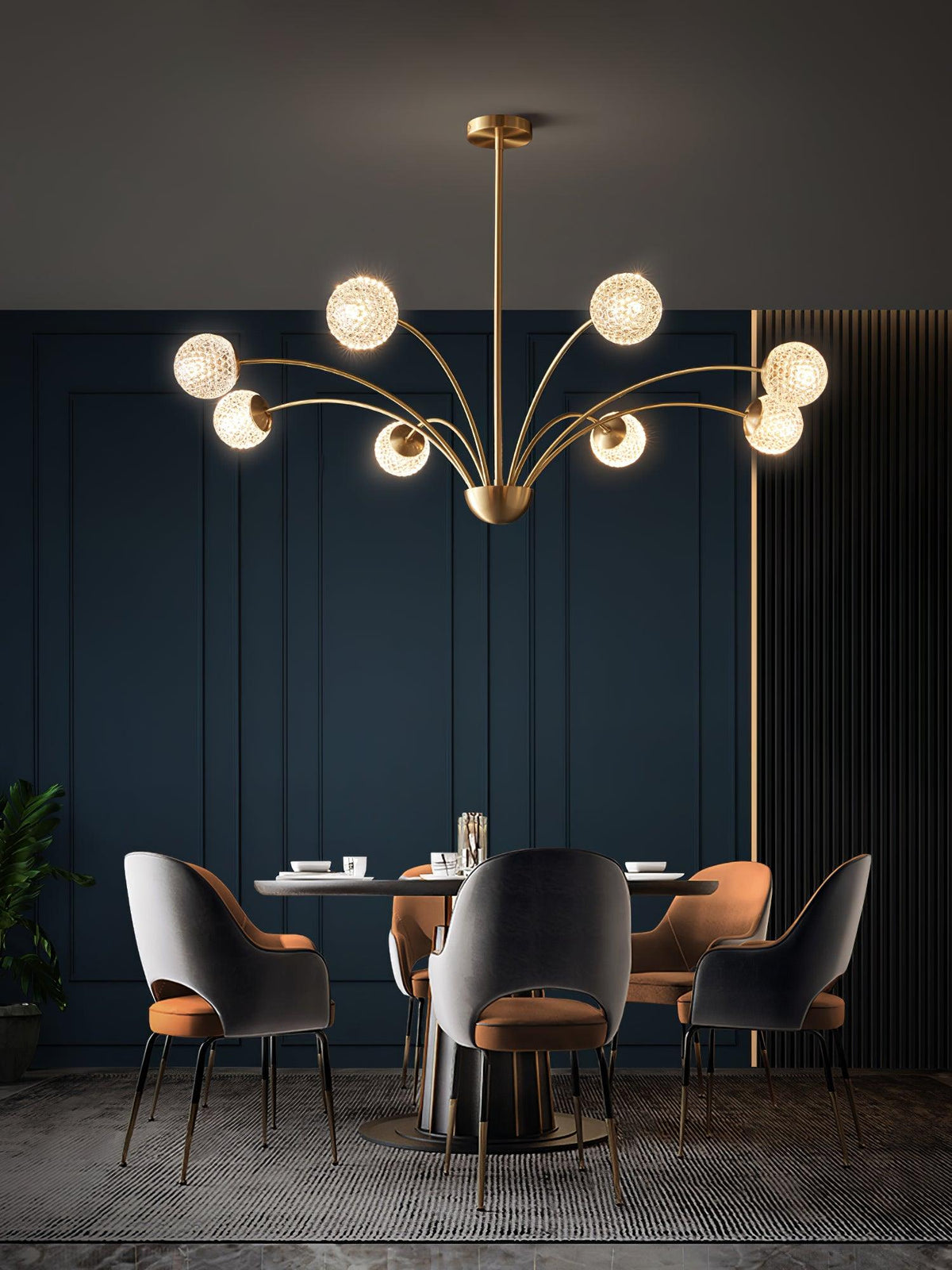 A Clérachic brass chandelier with textured globes over a dining table with grey and orange chairs, in a deep navy panelled room.