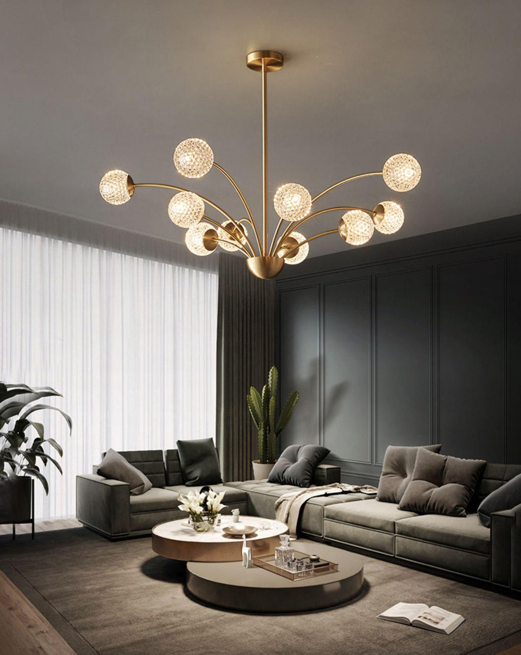 A Clérachic brass chandelier with textured globes over a round coffee table, in a grey living room with tall sheer curtains.