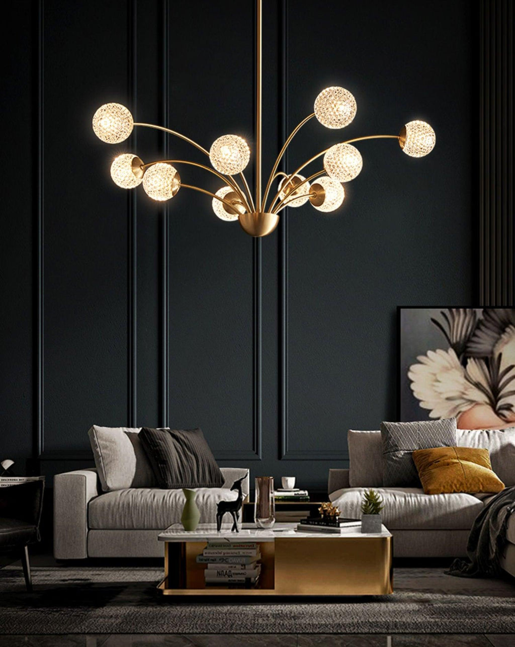 A lit Clérachic chandelier with textured globes in a charcoal room, with grey sofas, a brass-edged coffee table and a floral artwork.